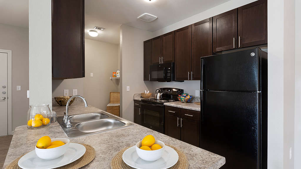 Model apartment kitchen with black appliances and chocolate brown cabinetry at The Oaks at Ben White
